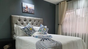 A neatly made bed with striped bedding, a tufted headboard, and pillows with geometric patterns. - Posh 3 Bed Guesthouse in Hillside With Pool - 2039 (Bulawayo)