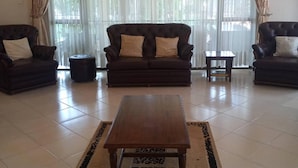Un salon avec un canapé marron foncé, deux fauteuils, une table basse en bois et un tapis à motifs.