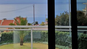 Vista a través de una ventana con un candelabro decorativo, cielo despejado y una lejana vista del mar.