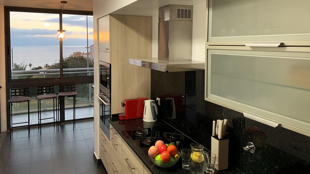 Una cocina moderna con un amplio ventanal, vista al mar, y un comedor con mesa y sillas.