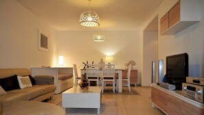 Una sala de estar moderna con un sofá, una mesa de centro, una mesa de comedor, sillas y un televisor.