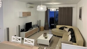 Una sala de estar moderna con un sofá color beige, una mesita de centro, un televisor y un mueble blanco.