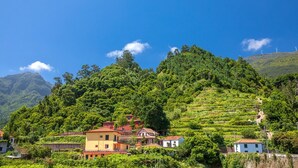 A hillside village with terraced vineyards, traditional houses, and wind turbines in the background. - Vila do Largo A by Homie (São Vicente)