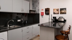 A modern kitchen with a black countertop, white cabinets, and a small island. There are two coffee makers, a kettle, and a fire extinguisher on the wall. - Vila do Largo A by Homie (São Vicente)