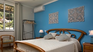 A bedroom with a wooden bed, a hanging clothes rack, and decorative wall art. - Vila do Largo A by Homie (São Vicente)