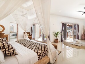Relax in a serene bedroom with a large bed under a canopy, a nightstand, mirror, and dresser, plus a view of the outdoor area.