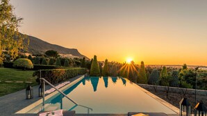 An infinity pool with a view of the sunset, surrounded by neatly trimmed hedges and a mountain in the background. - Luxury Villa Golden Crest With Private Swimming Pool (Hersonissos)