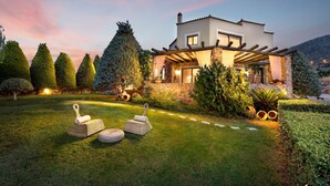 A modern house with a stone facade, a covered patio, and a well-maintained garden with hedges and trees. - Luxury Villa Golden Crest With Private Swimming Pool (Hersonissos)