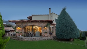 A stone house with a patio, outdoor seating, and a large evergreen tree. - Luxury Villa Golden Crest With Private Swimming Pool (Hersonissos)