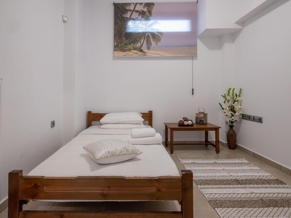 Une chambre à coucher bien rangée, avec un lit en bois, une petite table de chevet ornée d’un vase de fleurs et un tableau accroché au mur.