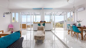 A spacious living area with a sofa, ottoman, and dining table with chairs. - Olive Tree Villa by Estia (Corfu)