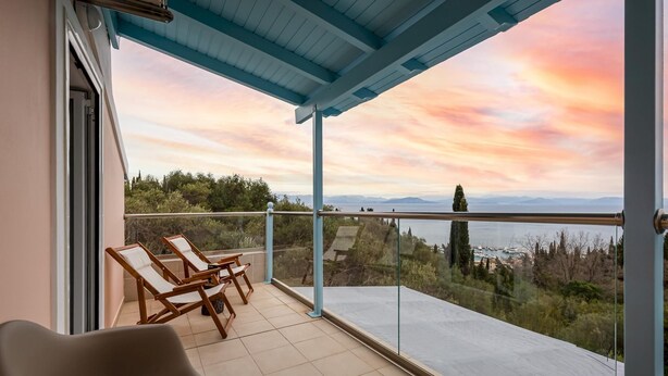 A balcony with a view of the sea and mountains, wooden chairs, and a glass railing. - Olive Tree Villa by Estia (Corfu)