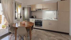 A compact kitchen with a dining area, featuring a round table, chairs, a refrigerator, an oven, and a sink. - Yialos Cohili Beach Residence by Estia (Hersonissos)