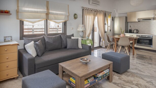 A modern living room with a grey sofa, a wooden coffee table, and a dining area with a table and chairs. - Yialos Cohili Beach Residence by Estia (Hersonissos)