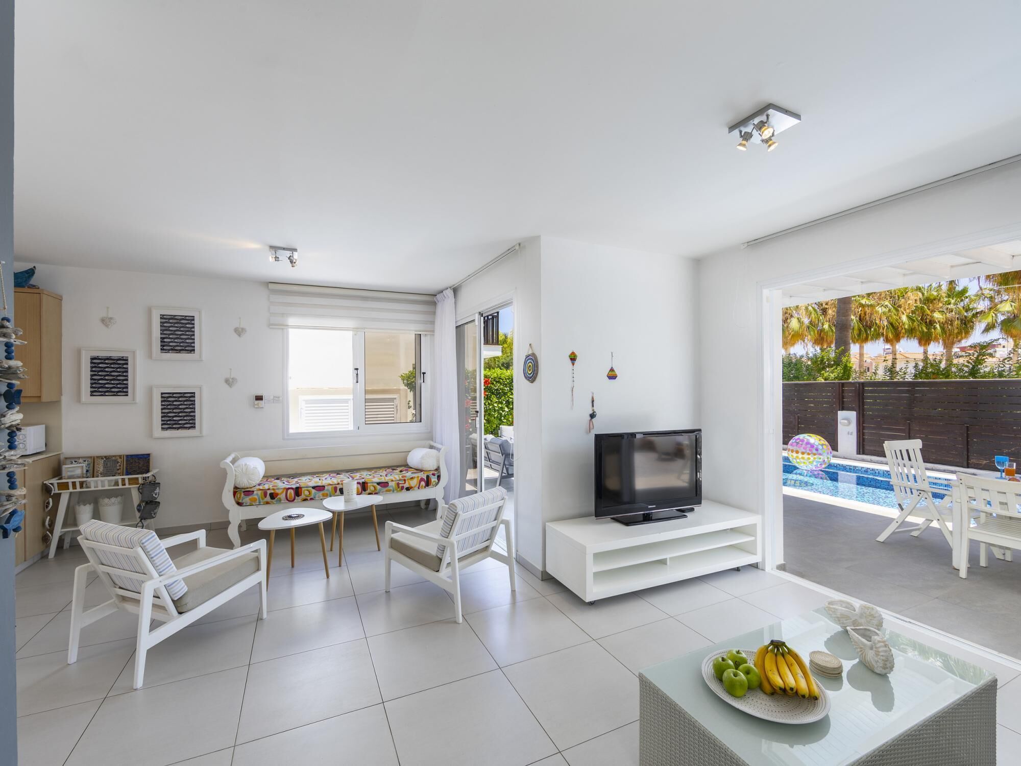 A modern living room with a TV, seating area, and a glass table with fruit.
