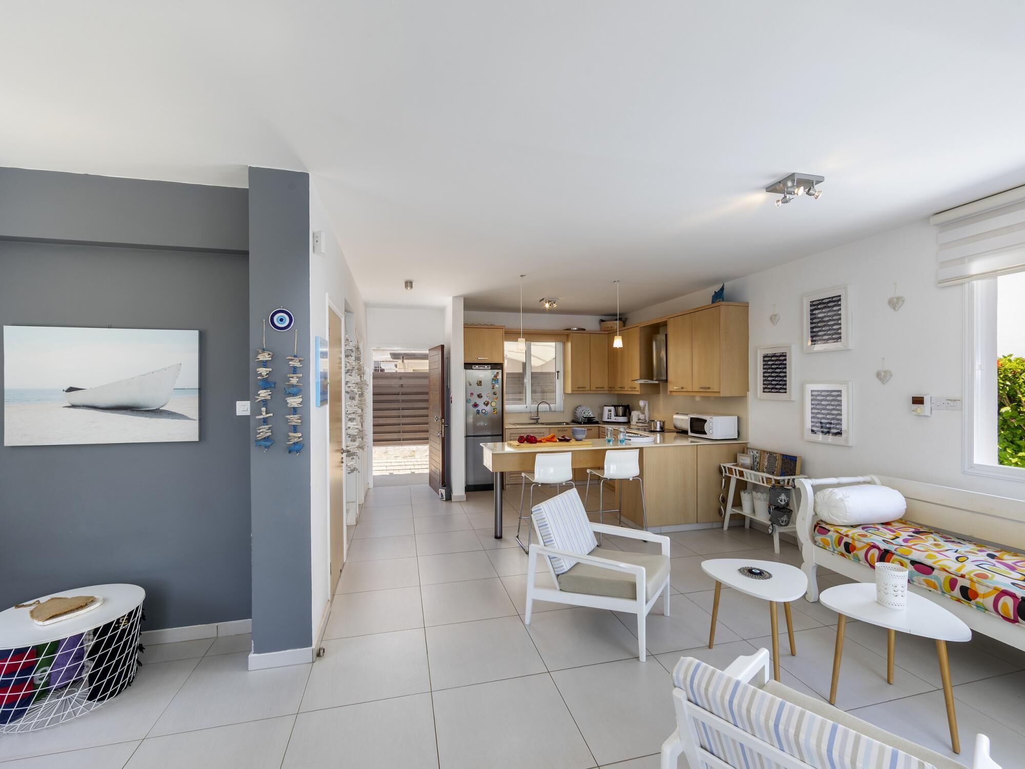 A modern kitchen with wooden cabinets, a dining area with white chairs, and a large window providing natural light.