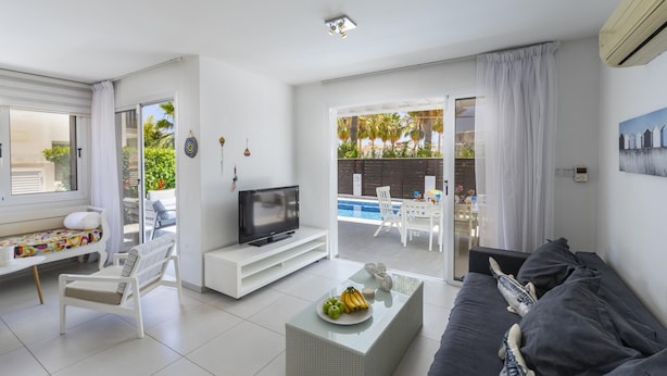 Ein modernes Wohnzimmer mit Fernseher, Sitzgelegenheiten, Blick auf einen Pool und einem Balkon.