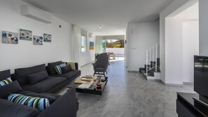 Una sala moderna con un sofá, una mesa de centro con juegos de mesa y un televisor. Se ve una escalera que conduce a un balcón con vistas.