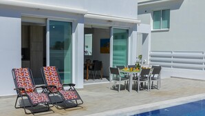 Un área de piscina moderna al aire libre con sillones, una mesa de comedor y vista despejada a la piscina.