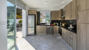 Una cocina moderna con armarios de madera, electrodomésticos de acero inoxidable y un amplio ventanal corredero que da a un espacio exterior.