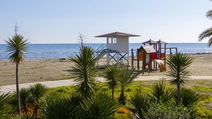 A lifeguard tower and playground on a beach with palm trees and a clear sky. - Mackenzie Castella Beachfront Suite (Larnaca)