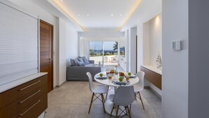 A modern dining area with a round table, white chairs, and a view of the beach. - Mackenzie Castella Beachfront Suite (Larnaca)
