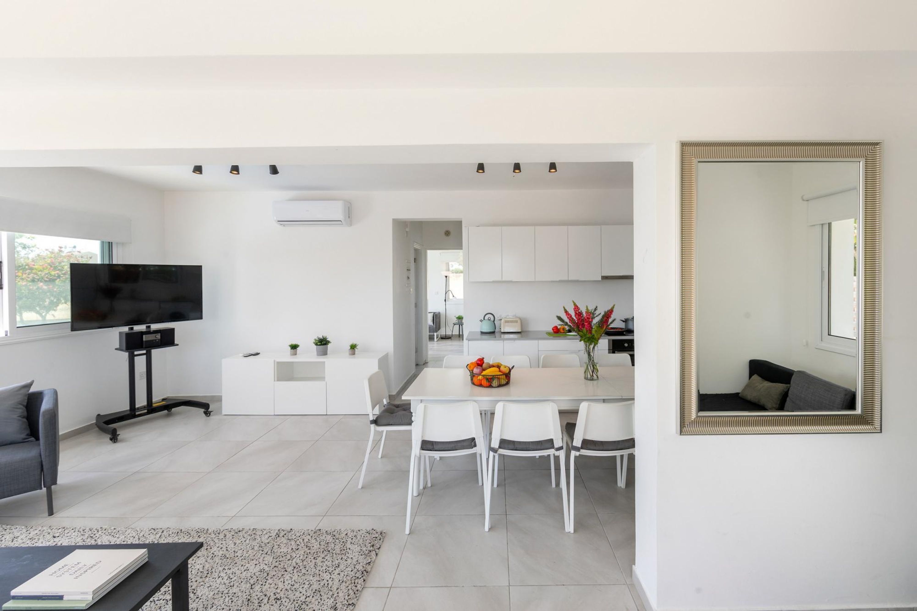 A modern, open-plan living space with a dining area, kitchen, and a large mirror.