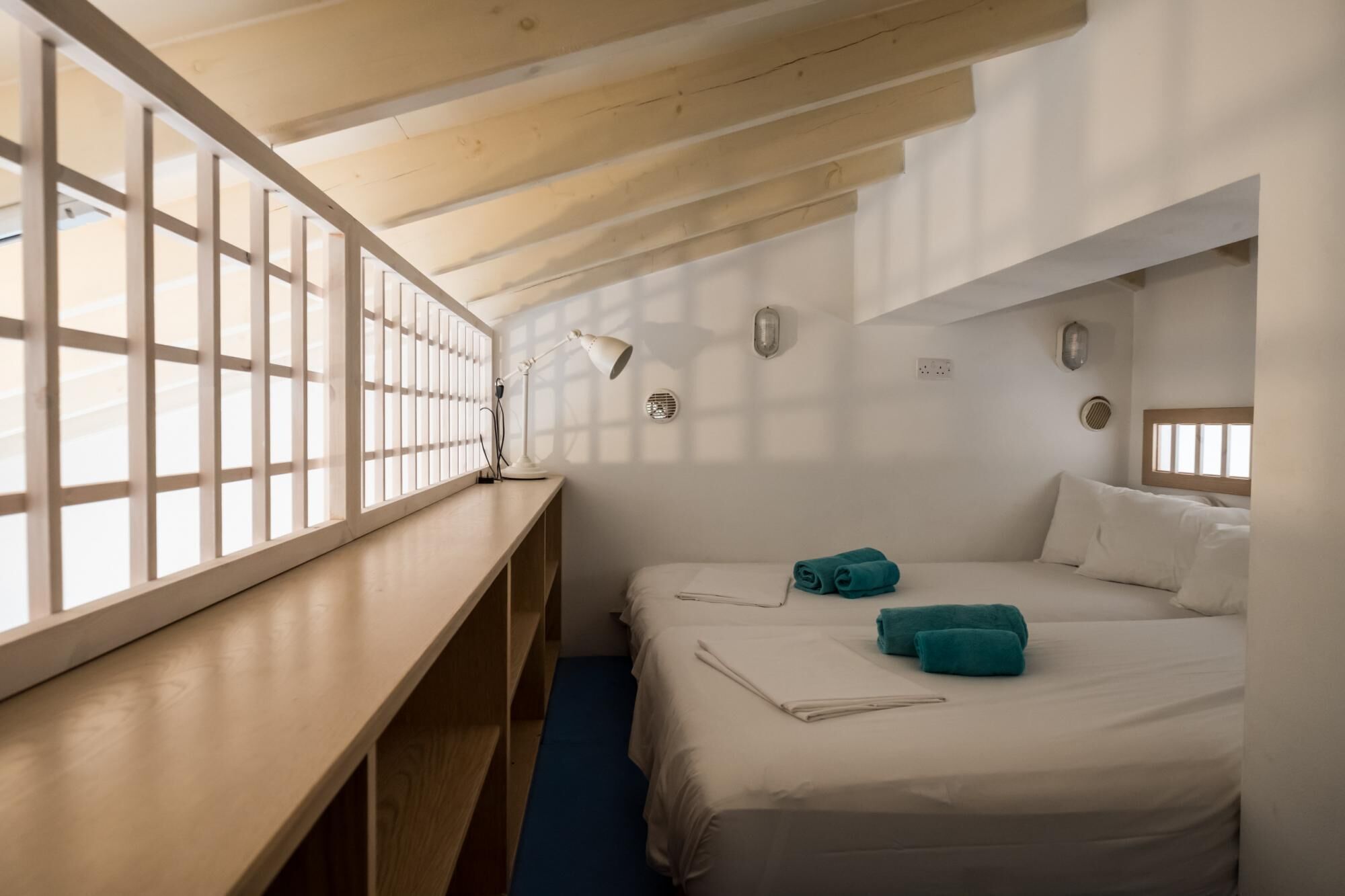 A room with two beds, a desk, and a window with blinds.