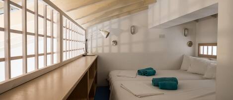 A room with two beds, a desk, and a window with blinds.