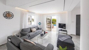 Ett modernt vardagsrum med en soffa, ett soffbord, en tv och ett stort fönster.
