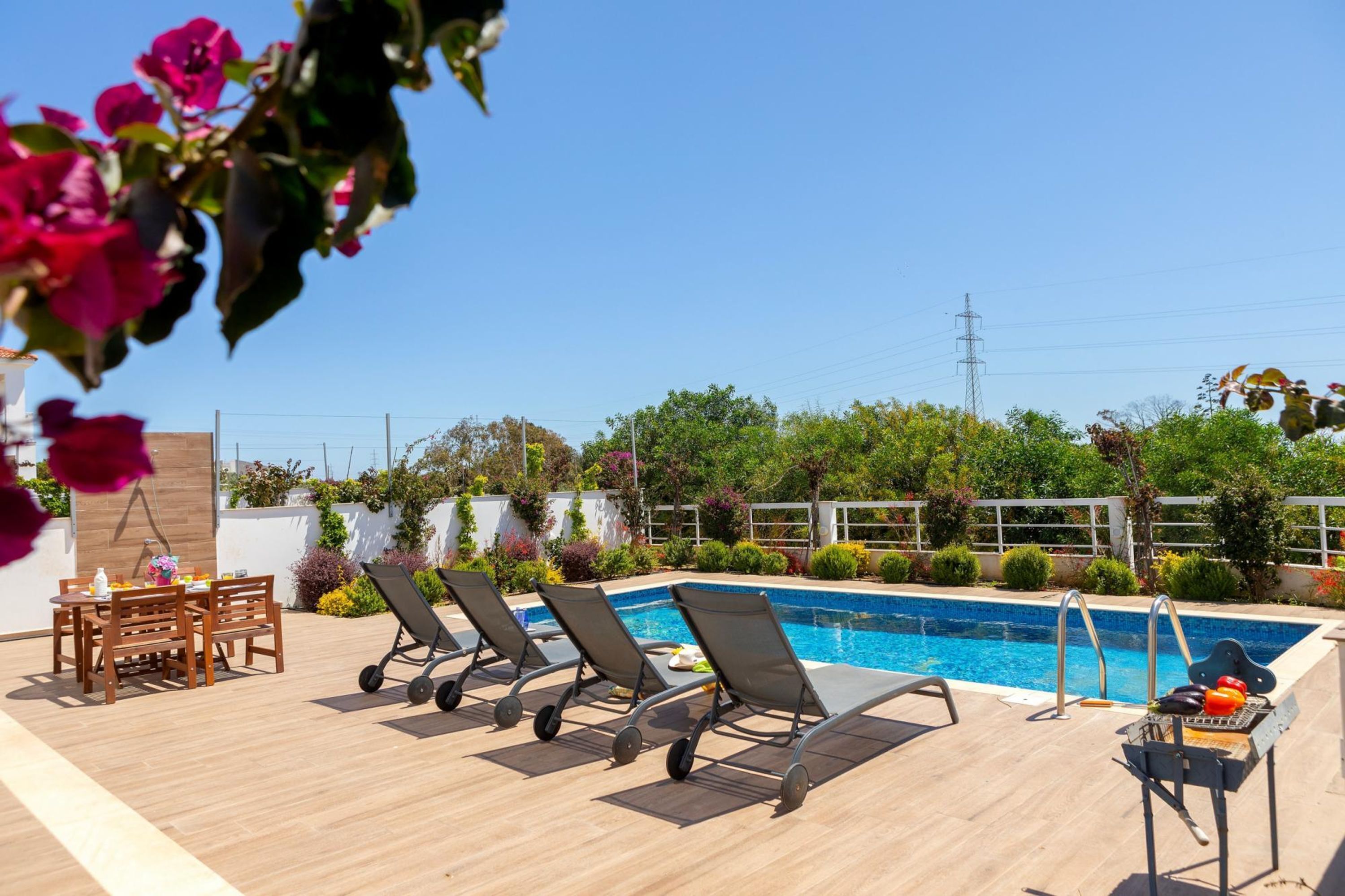 A poolside area with lounge chairs, a table with drinks, and a grill.