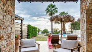 A patio with wooden furniture, a glass table, and a view of a pool and palm trees. - Palmrise Luxury Villas - Maistros Villa (Kassandra)