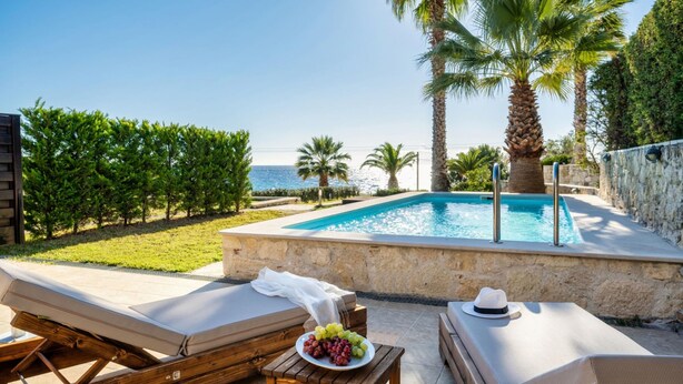 A poolside area with lounge chairs, a small table with a plate of grapes, and a view of the sea. - Palmrise Luxury Villas - Maistros Villa (Kassandra)