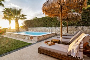 A poolside area with a rectangular pool, lounge chairs, and a thatched umbrella. - Palmrise Luxury Villas - Maistros Villa (Kassandra)