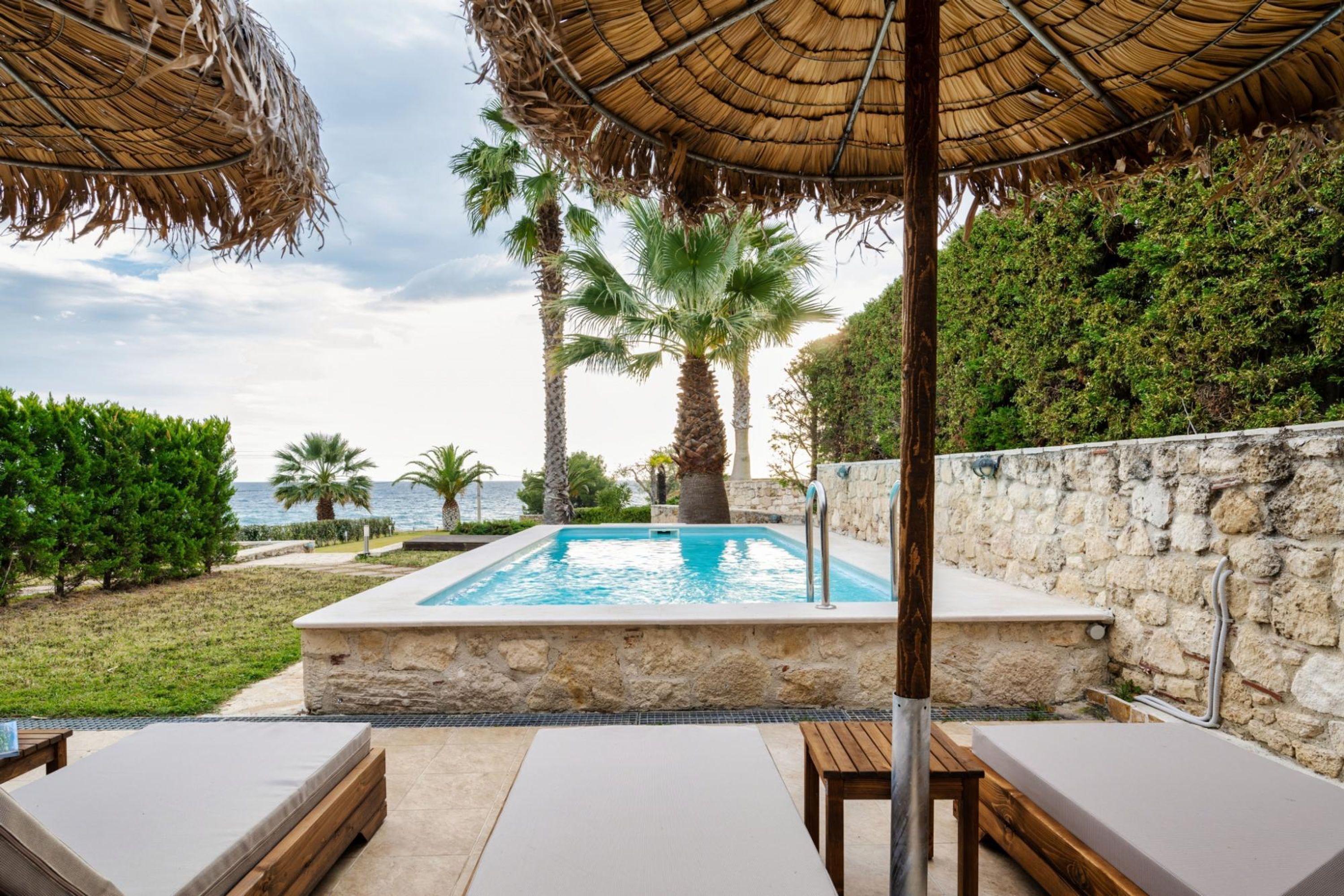 Un espace piscine agrémenté de chaises longues, d’un mur en pierre et de palmiers.
