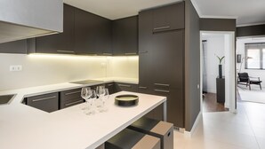 A modern kitchen with dark cabinets, a white countertop, and a built-in island with glasses and plates. - Executive 2 bdr Suite in Plaka - Acropolis View (Athens)