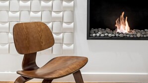 A modern interior with a white textured wall, a flat-screen TV mounted above a fireplace, and a wooden chair in front. - Executive 2 bdr Suite in Plaka - Acropolis View (Athens)