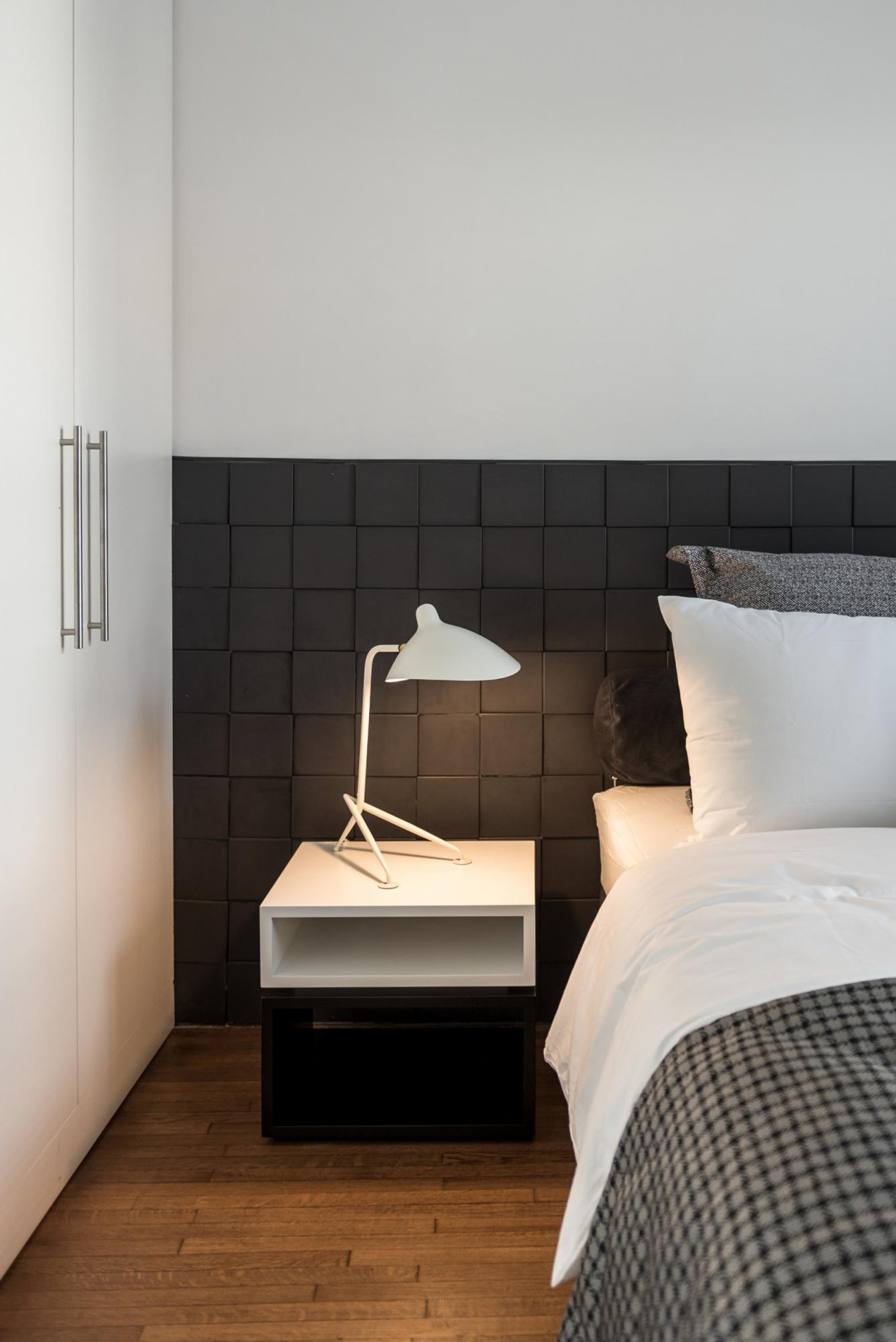 A bedroom with a bed, a bedside table with a lamp, a black headboard, and a wooden floor.