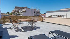 A rooftop terrace with a table and chairs, a view of buildings, and a flag. - Downtown Cocoon With Roof Deck (Athens)