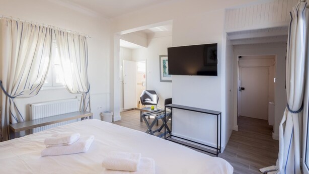 A hotel room with a bed, a desk, a chair, a TV, and a bathroom door. - Downtown Cocoon With Roof Deck (Athens)