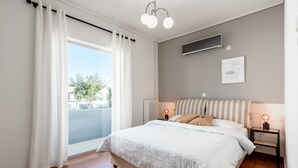 Un dormitorio con una cama grande, una ventana con cortinas, una mesita de noche con lámpara y un aire acondicionado instalado en la pared.