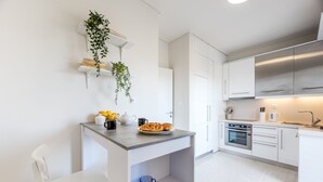 Una cocina moderna con armarios blancos, horno empotrado y una encimera con comida y un hervidor.