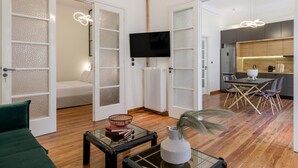 A modern living room with a sofa, a coffee table, and a TV. There is a kitchen area with a dining table and chairs. - 3bdr Modern Design Bright Interiors in Plaka (Athens)
