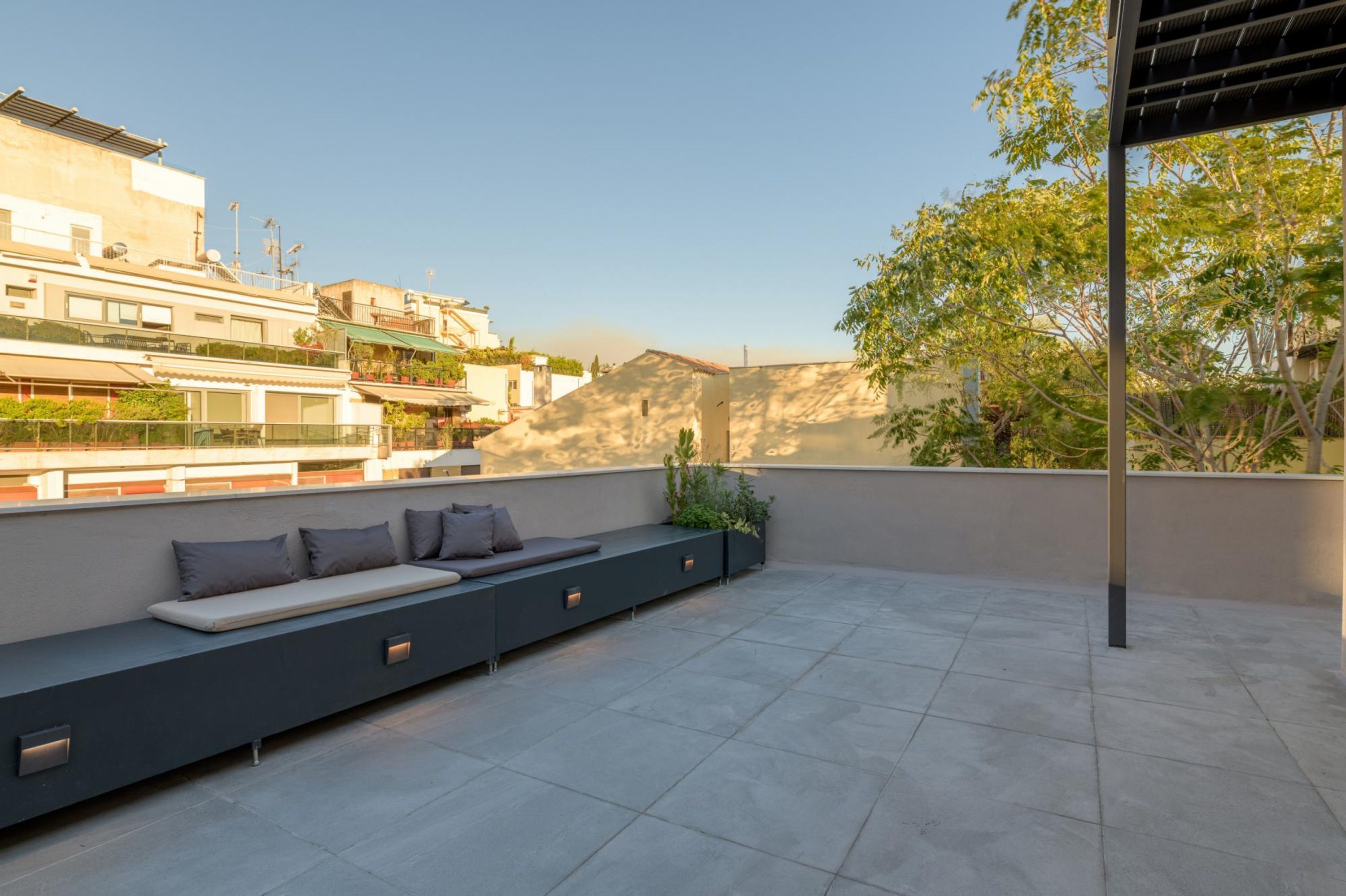 A rooftop terrace with a long bench, potted plants, and a pergola.