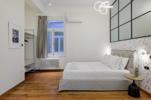 Une chambre moderne avec un grand lit, un radiateur, une fenêtre avec des rideaux, une table de chevet avec une lampe et un mur orné de motifs géométriques.