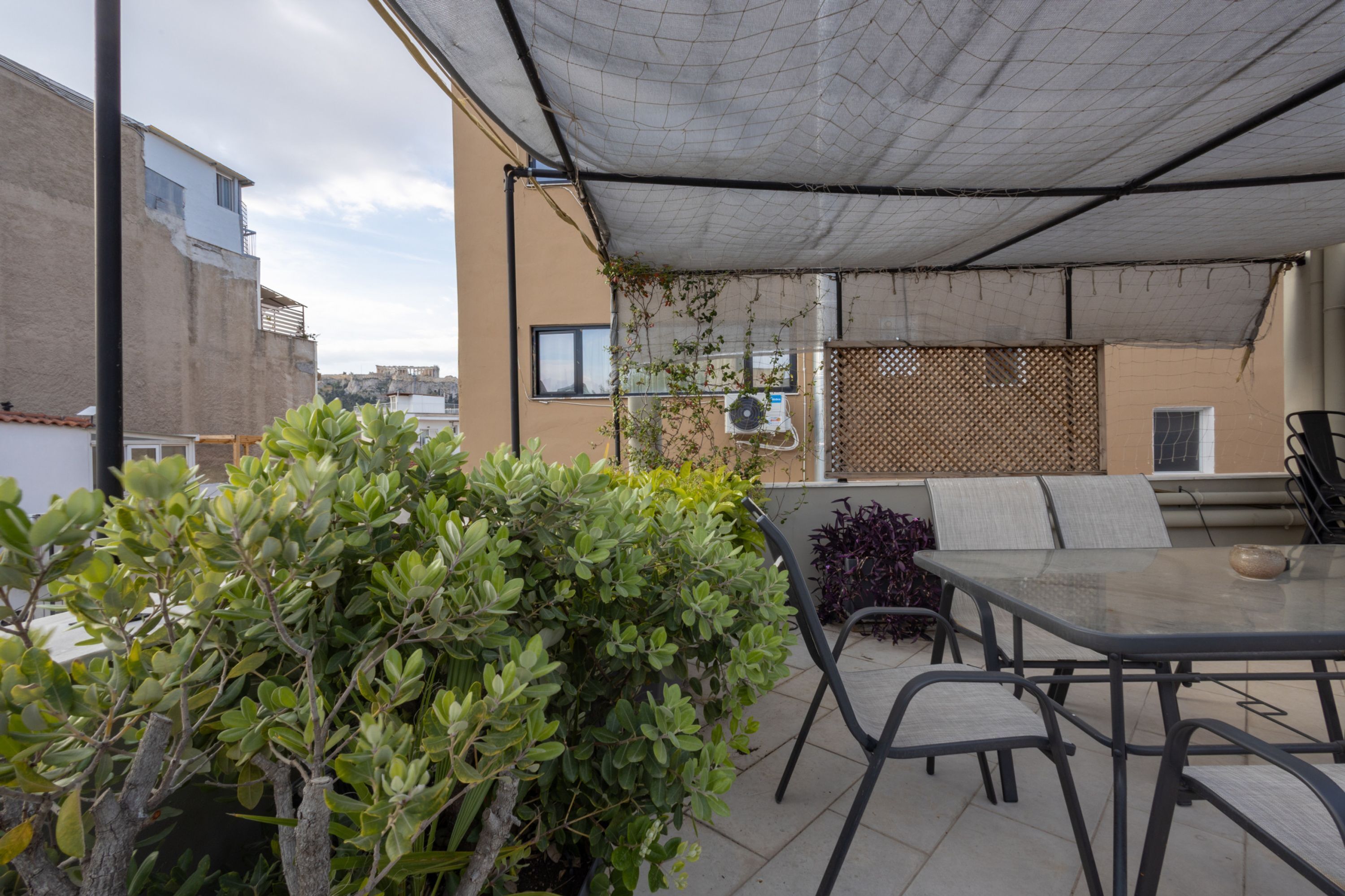 An outdoor patio with a table and chairs, surrounded by greenery and a shaded area.