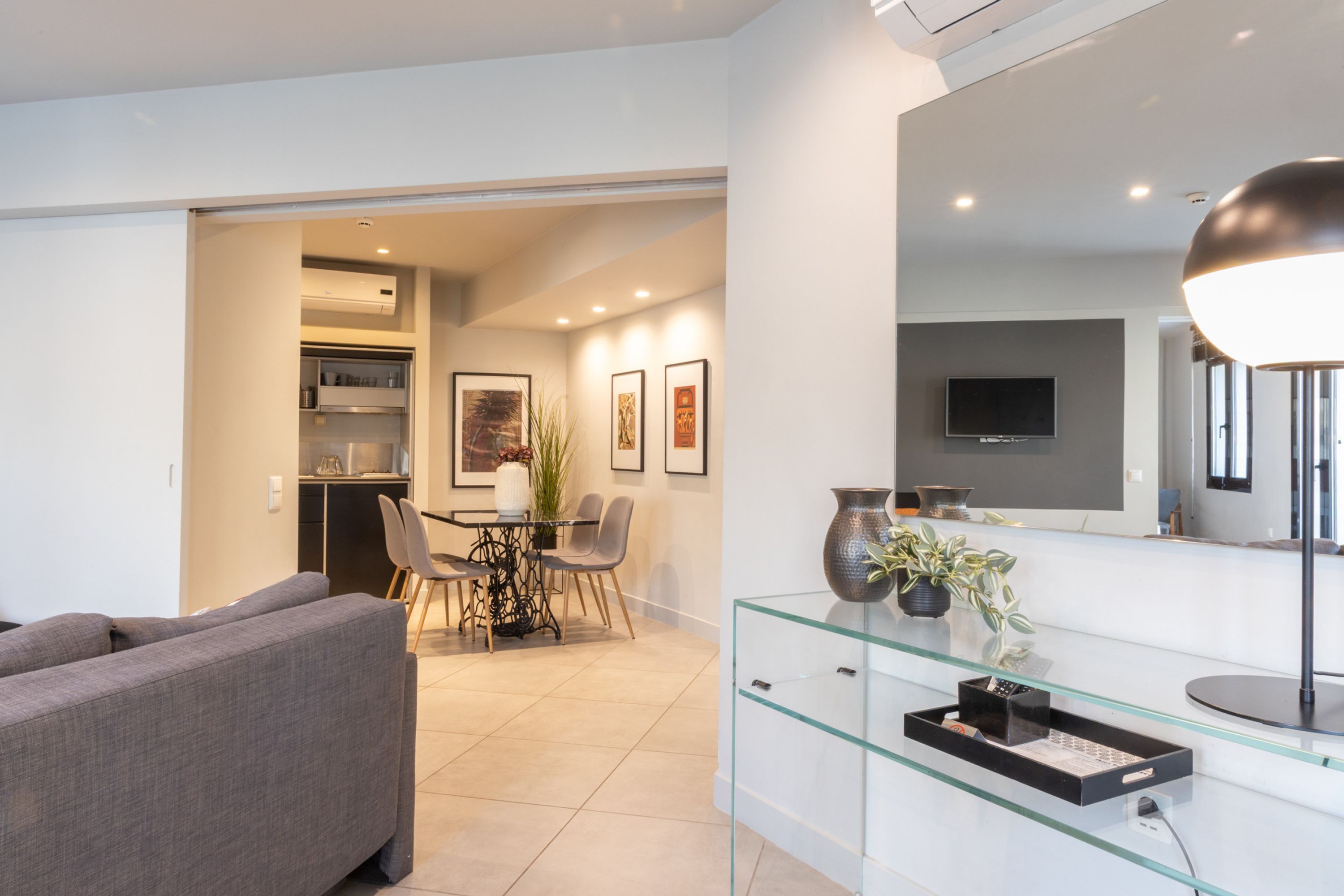 A modern living room with a sofa, a glass coffee table, and a dining area with chairs and a table.
