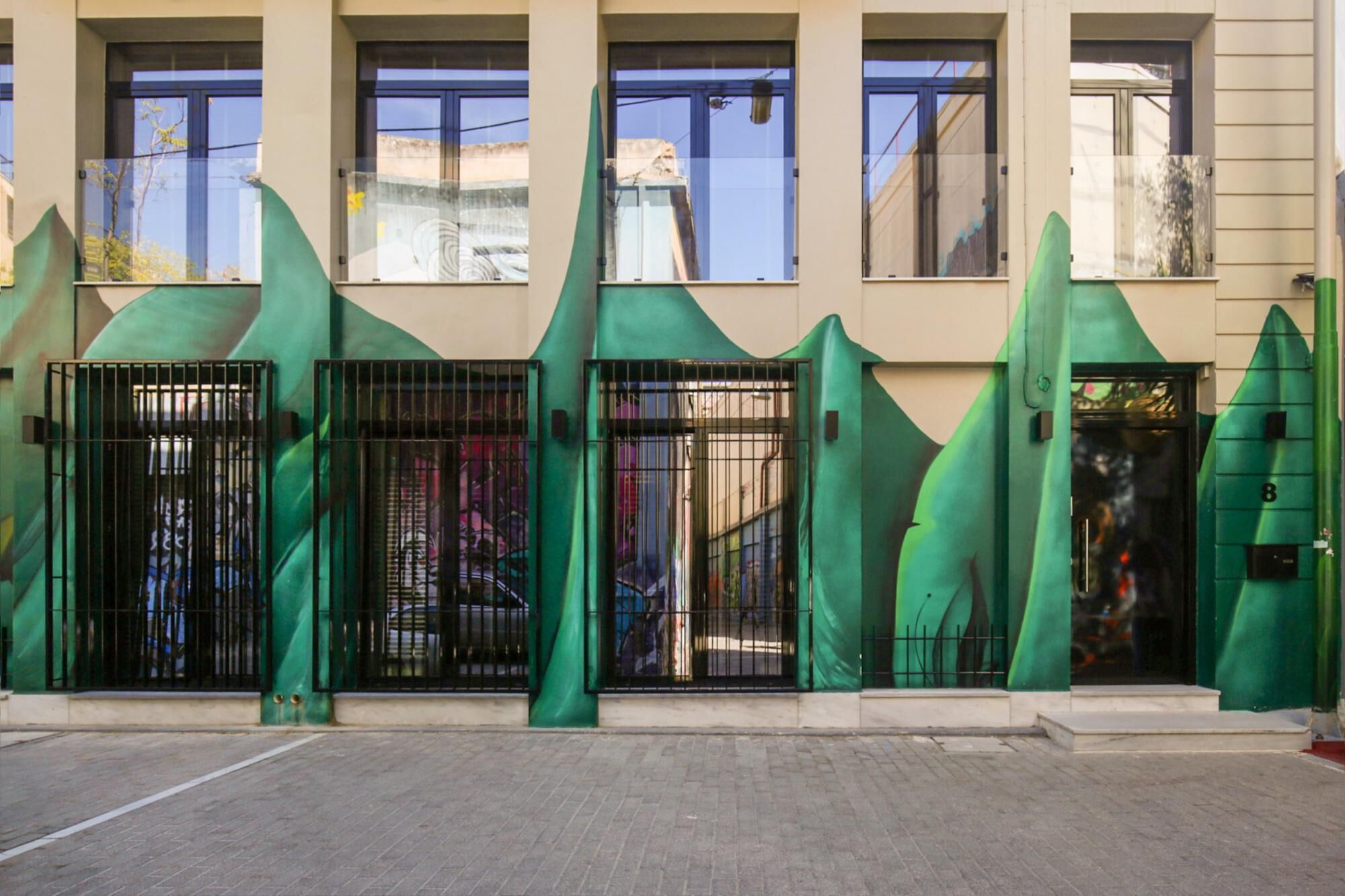 Facciata di un edificio con tre strutture verdi a forma di onda e cancelli neri.