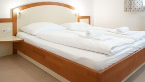 A double bed with white linens and towels, a wooden headboard, and a bedside table with a lamp.