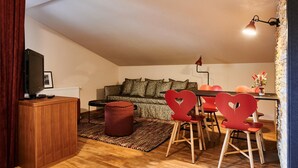Un espacio habitable estilo loft acogedor, con piso de madera, un sofá, una mesa de comedor con sillas rojas y un televisor sobre un mueble de madera.